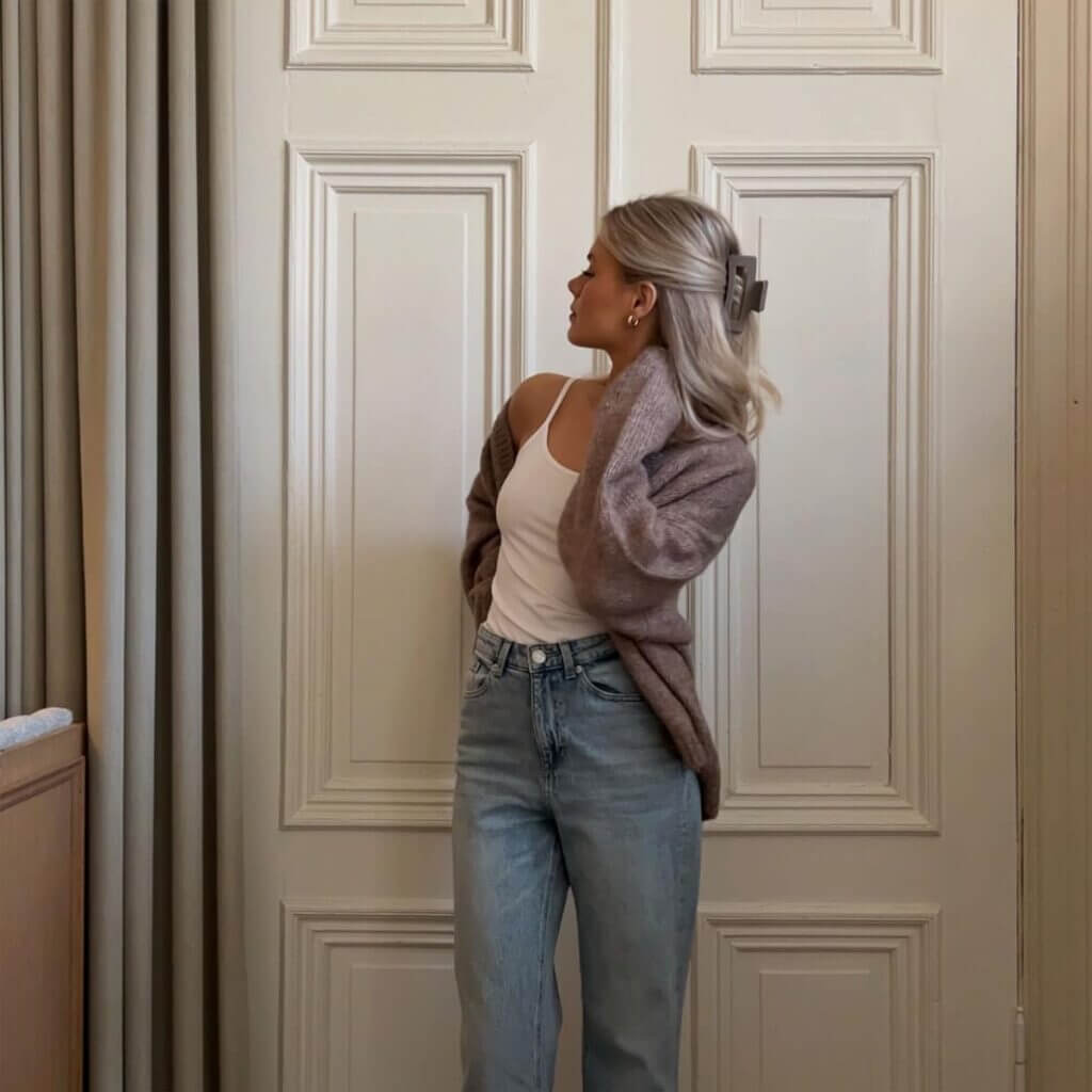 Ljusgrå large-hårklämma – stylad i blont hår på modell i brun kofta, vita dörrar i bakgrunden