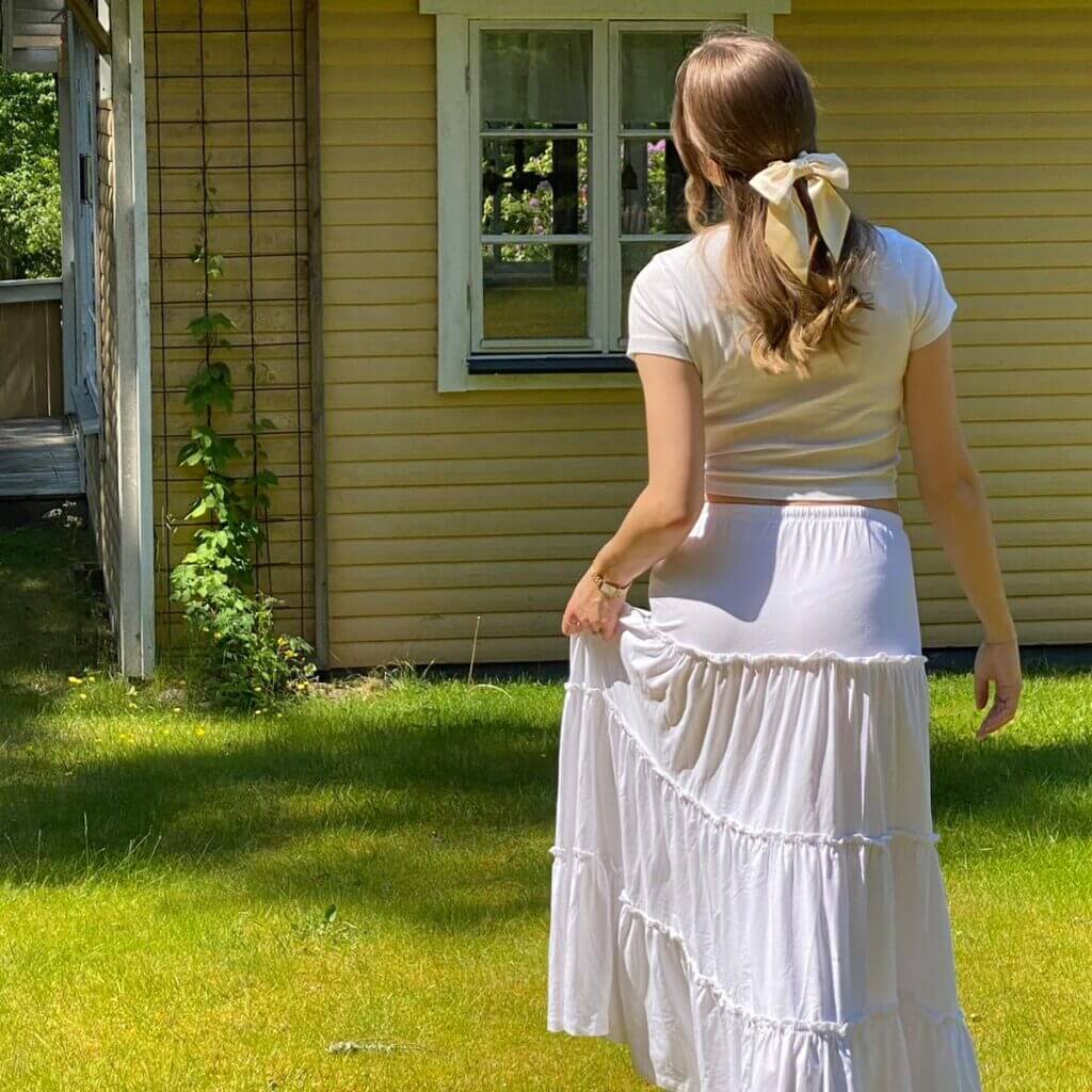 Champagnefärgad scrunchie med sidenrosett i halvt utsläppt hår – sommarlook framför gul trähusvägg